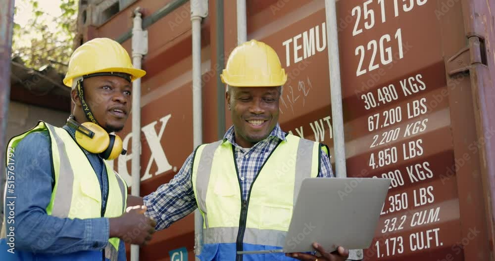 team of African-American container workers use their laptops to inspect shipping containers. Wear a hardhat to be safe at work. professional collaboration. transportation of goods team of African-American container workers use their laptops to inspect shipping containers. Wear a hardhat to be safe at work. professional collaboration. transportation of goods