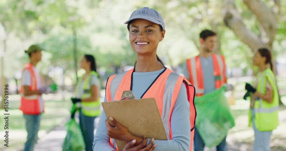 Female volunteer with a clipboard in the park leading a group of responsible activists doing charity work by cleaning up litter in the community. Caring for a sustainable, clean and safe environment