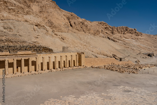 Fragment of the funerary temple of the queen-Pharaoh Hatshepsut on the background of a steep cliff. An ancient colonnade and a brick wall are visible. Clear blue sky. Egypt. Luxor