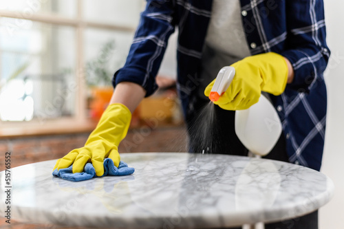 Close up hand of woman wearing yellow gloves cleaning marble stone table using clothes and cleaning solution.