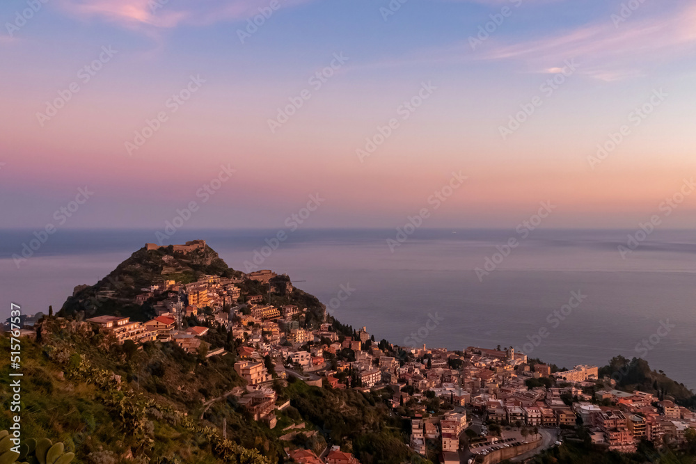 Panoramic view during sunset on coastline of Ionian Mediterranean sea, Taormina, Sicily, Italy, Europe, EU. Twilight over Saracen castle on the hills of tourist town Taormina. Vibrant sky calm colors