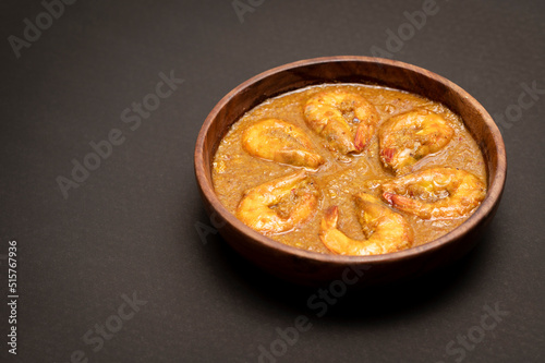 Bengali Dish or Food - Delicious authentic Bengali Prawn Malai Curry also known as chingri malai curry served on a wooden bowl. Traditional Goan Prawns or Shrimp curry. top view black background.