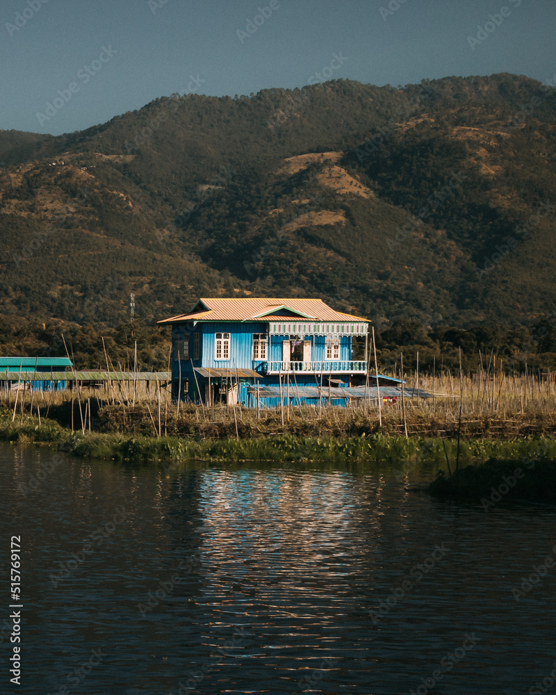 Naklejka premium Burmese style blue wooden house on Inle Lake in Myanmar on a sunny day with mountains in the background. 