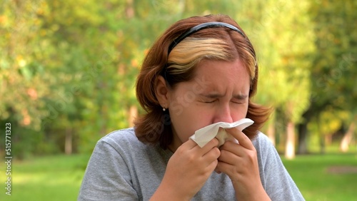 A young girl with allergies in an autumn park. Sneezing girl blows her nose into a napkin and sneezes. selective focus