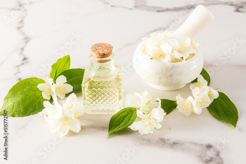 glass vial with organic jasmine oil, mortar and pistil with flowers on a marble white background. the concept of natural oils.