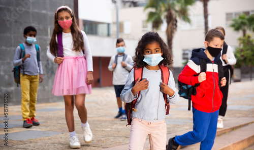 Schoolchildren in masks walking together on the street from school at day