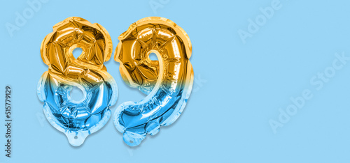 Rainbow foil balloon number, digit eighty nine on a blue background. Birthday greeting card with inscription 89. Top view. Numerical digit. Celebration event, template. Banner photo