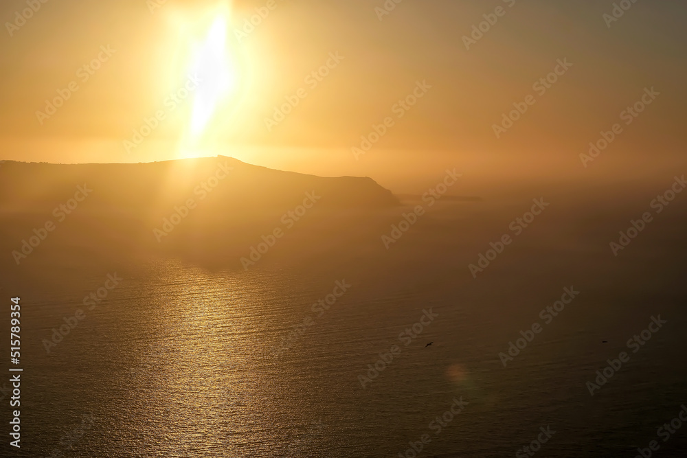View of the sun slowly setting behind the volcano of Santorini and producing a spectacular sunset