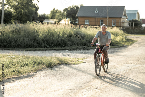 an elderly man rides a bicycle in the village. Grandpa leads a healthy lifestyle.
