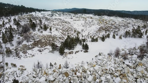 A winter landscape in the mountains. Travellers explore an abandoned marble quarry surrounded by coniferous forest. Huge blocks of light stone are stacked around it. The concept of sport and tourism.