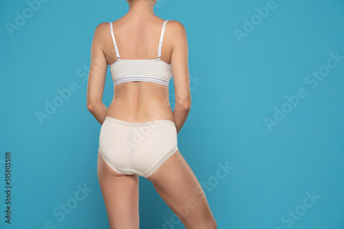 Torso of woman wearing white briefs and sport bra, backt view on a blue background