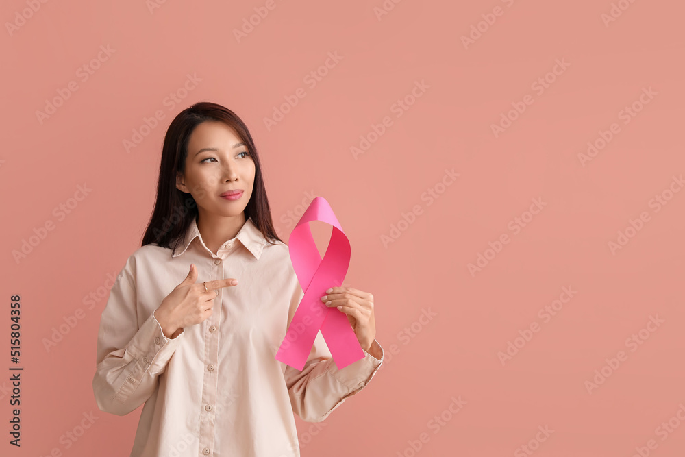 Young Asian woman with pink ribbon on color background. Breast cancer awareness concept
