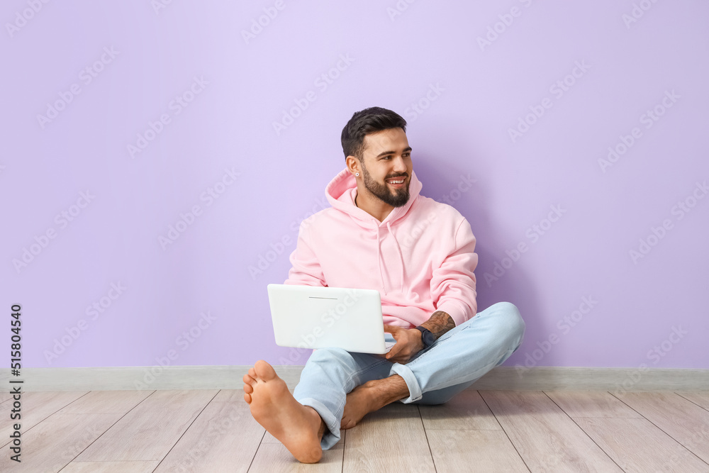 Handsome barefoot man using laptop near lilac wall Handsome barefoot man using laptop near lilac wall