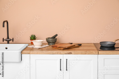 Cutting boards, mortar with pestle and colander on counter near beige wall © Pixel-Shot