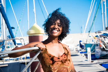 Tourist young black woman smile at the camera posing in summer holiday vacation. People and travel lifstyle. Ethnic girl cheers and look on camera in a sunny portrait at the harbour
