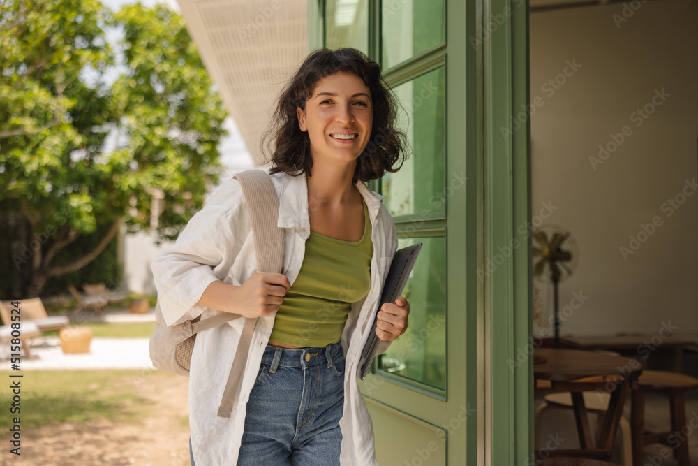 Cute young caucasian brunette girl goes to study with laptop and backpack. Brunette wears t-shirt, shirt and jeans. Concept of lifestyle, learning Cute young caucasian brunette girl goes to study with laptop and backpack. Brunette wears t-shirt, shirt and jeans. Concept of lifestyle, learning