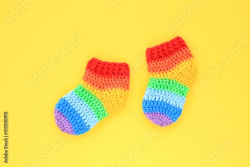 Rainbow handmade crochet gift socks booties on yellow background. Happy motherhood, pregnant, newborn idea. Baby shower greeting card, poster, banner topview concept. Flatlay with copy space. Close up
