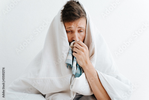 Fototapeta Sick sad man with symptoms of runny nose wrapped in warm blanket and holding handkerchief