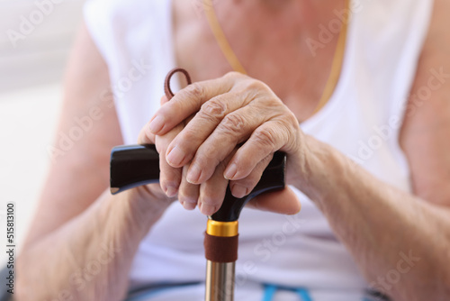 Senior female sitting and putting hands on supporting stick