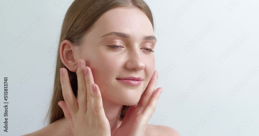 A beautiful young woman applies a cream, makes a face massage while looking in the mirror. The concept of caring for clean and healthy female skin. A beautiful young woman applies a cream, makes a face massage while looking in the mirror. The concept of caring for clean and healthy female skin.