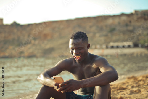 Fototapeta Naklejka Na Ścianę i Meble -  portrait of young man at the beach while using a smartphone