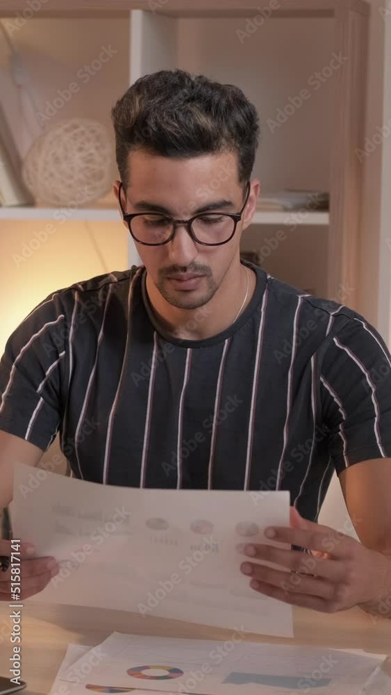 Vertical video. Remote job. Busy man. Data accounting. Concentrated guy studying financial report putting into laptop sitting desk light room interior. Vertical video. Remote job. Busy man. Data accounting. Concentrated guy studying financial report putting into laptop sitting desk light room interior.