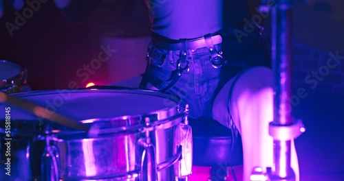 Beautiful female drummer praiseworthy playing drums in nightclub with big panoramic round window in twinkling concert RGB spot lights. Drummer girl concert concept. photo