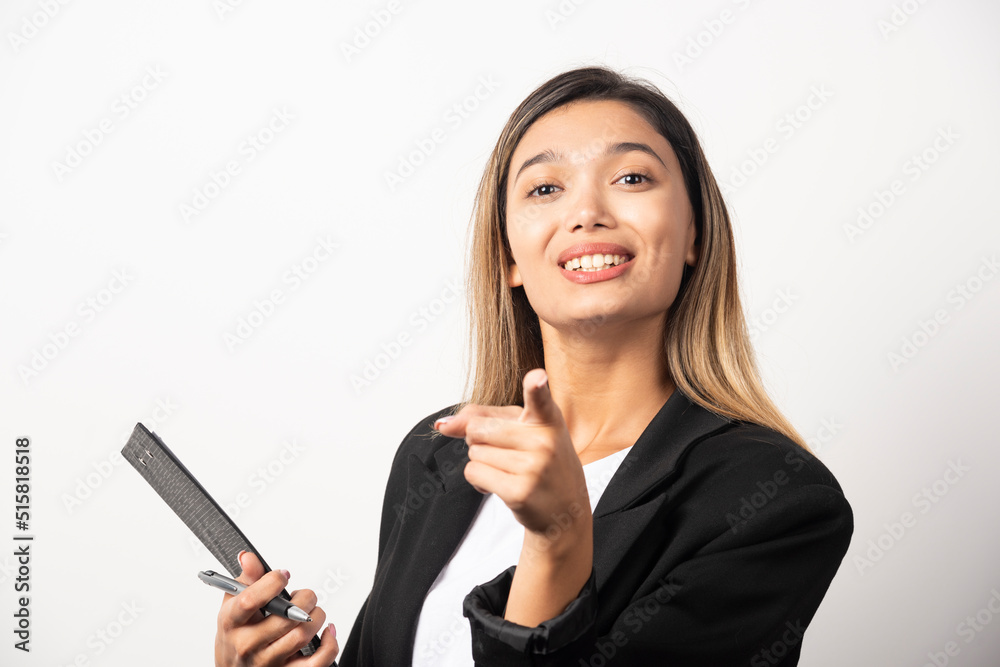 Young business woman holding clipboard and pointing at camera Young business woman holding clipboard and pointing at camera
