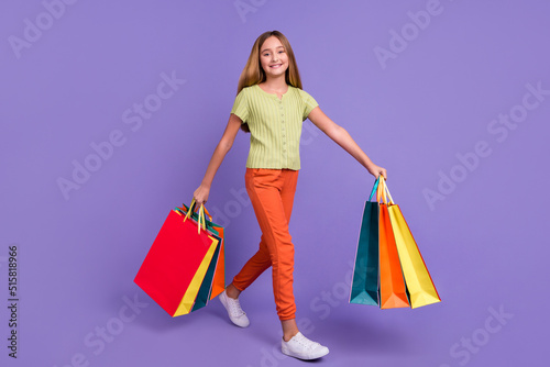 Full size profile photo of positive adorable girl hold packages walk isolated on violet color background