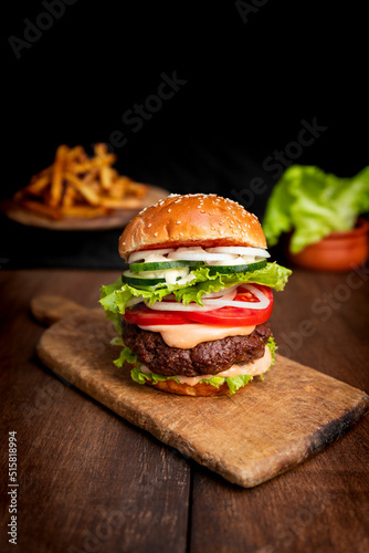 Burger with beef meat, cheese, lettuce, onion, tomato, cucumber, mayo and ketchup on an old wooden table. Junk food concept