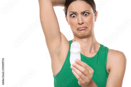a horrified young woman applies deodorant under her armpits on a white background