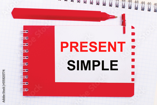 On a white notepad, a red pen, a red notepad and a white sheet of paper with the text PRESENT SIMPLE
