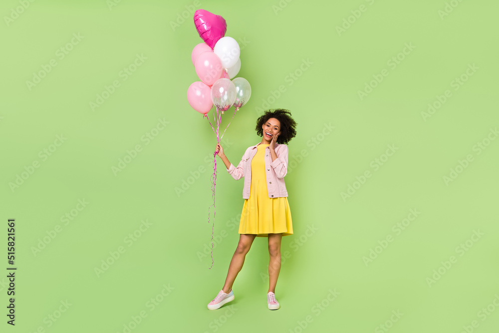 Full size photo of charming excited girl hand cheek hold balloons isolated on green color background