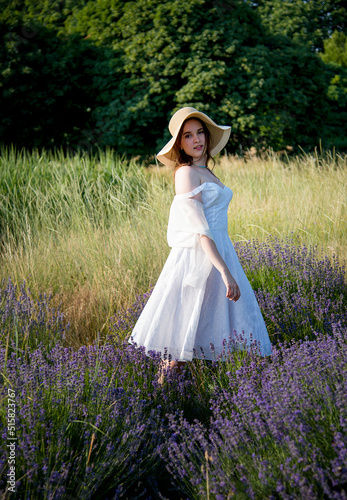 portrait of a beautiful sexy smiling woman  in straw hat and white dress walking in lavender field
