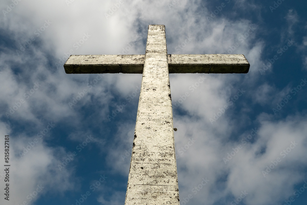 Tall Catholic cross against blue cloudy sky. Religion concept.