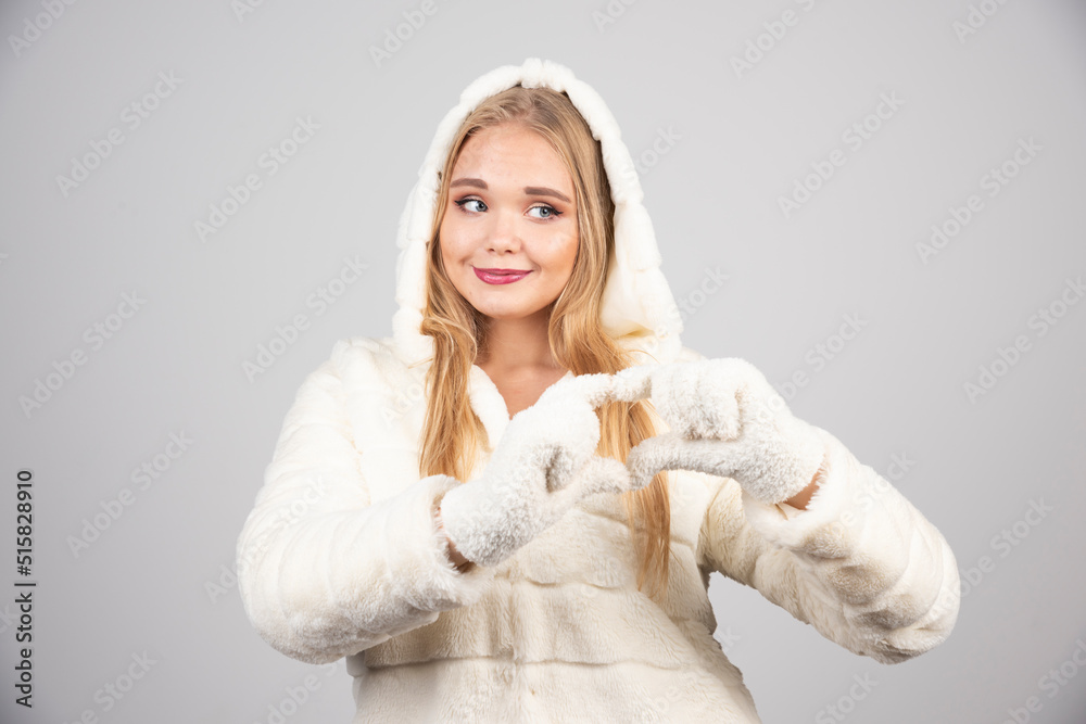 Blonde woman in winter outfit giving heart sign