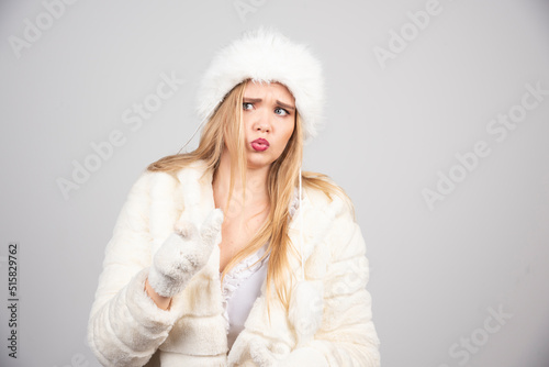 Young woman in winter jacket standing on gray background