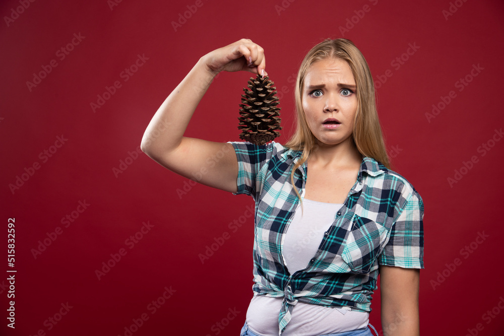 Blonde girl holds oak tree cone in the hand and gives surprized poses