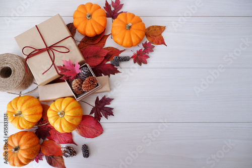 Autumn seasonal concept background. Autumn leaves, pumpkin and gift box on white wooden background. Thanks giving, Halloween and Autumn event decorative elements. 