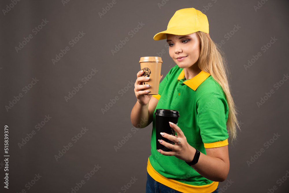 Smiling deliverywoman holding cups of coffee on dark background Smiling deliverywoman holding cups of coffee on dark background