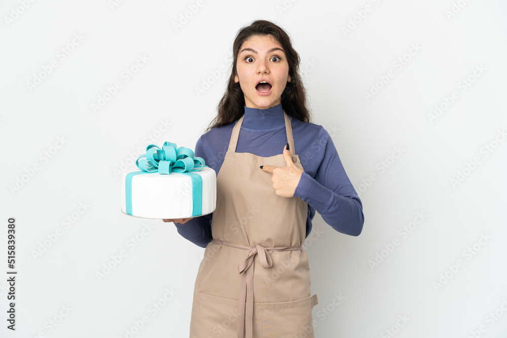 Pastry Russian chef holding a big cake isolated on white background with surprise facial expression Pastry Russian chef holding a big cake isolated on white background with surprise facial expression