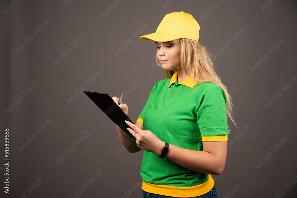 Young female courier with pencil looking on clipboard Young female courier with pencil looking on clipboard