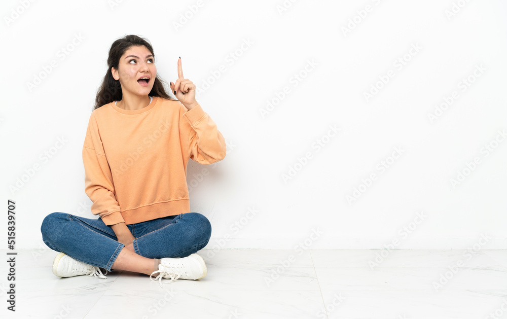 Teenager Russian girl sitting on the floor intending to realizes the solution while lifting a finger up Teenager Russian girl sitting on the floor intending to realizes the solution while lifting a finger up