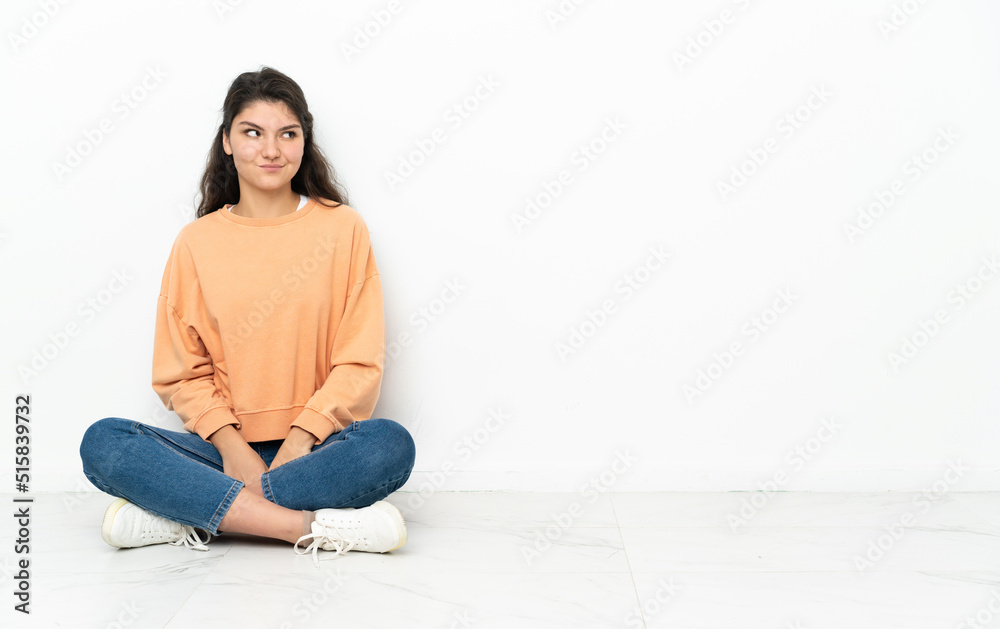 Teenager Russian girl sitting on the floor making doubts gesture looking side