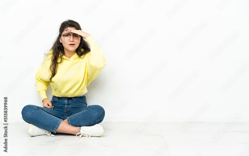 Teenager Russian girl sitting on the floor looking far away with hand to look something Teenager Russian girl sitting on the floor looking far away with hand to look something