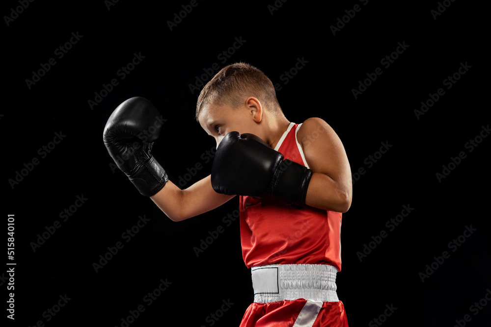 Young beginner boxer, sportive boy training isolated over dark background. Concept of sport, movement, studying, achievements, lifestyle.