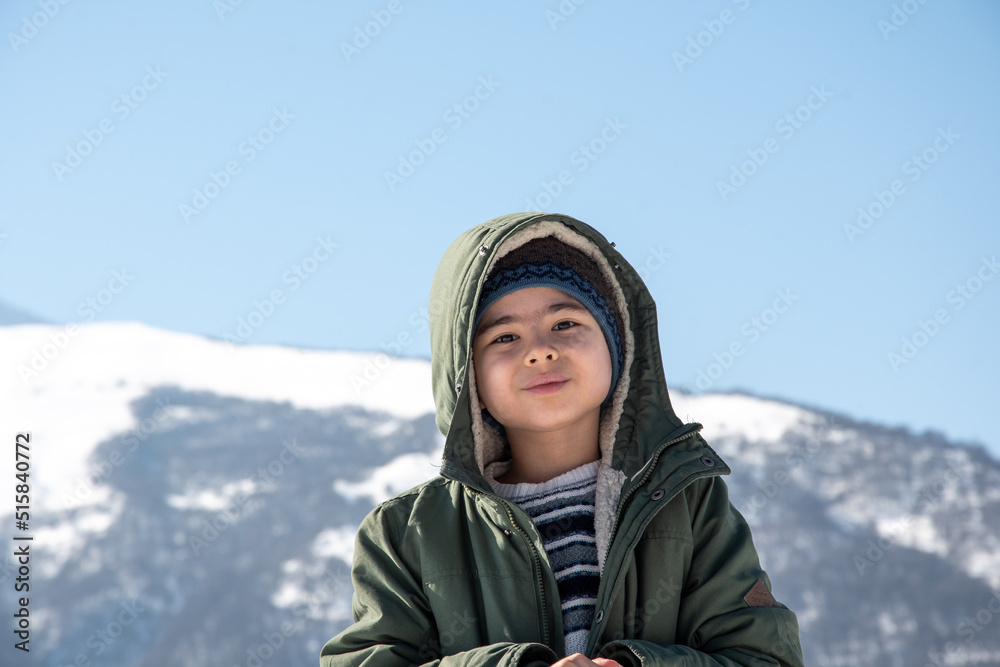 The boy stands in the winter in a green jacket against the backdrop of the mountains The boy stands in the winter in a green jacket against the backdrop of the mountains
