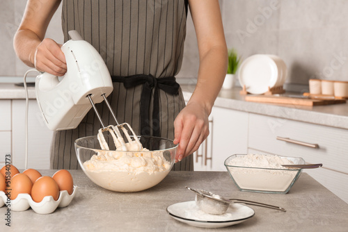 Fotótapéta Woman whipping white cream with mixer at light grey table in kitchen, closeup