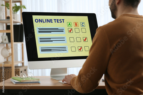 Man taking online test on computer at desk indoors, closeup