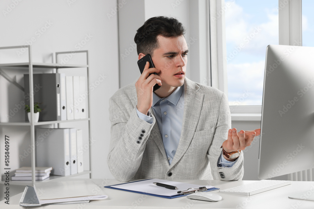 Confused businessman talking on phone while working in office Confused businessman talking on phone while working in office
